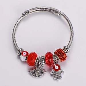 Detailed shot of silver evil eye and Hamsa hand charms on a beaded metal bracelet