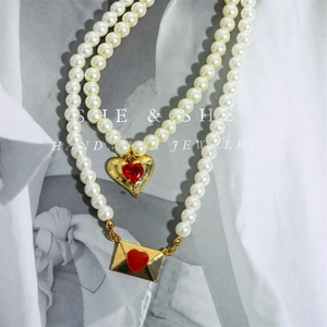 Detail of 18K gold-plated pearl necklace set with red heart and envelope pendants
