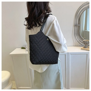 Gros plan d'un sac cabas noir matelassé avec logo doré porté par un mannequin en mouvement