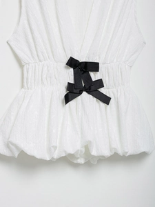 Détail d'un haut blanc à col en V avec nœuds noirs et taille plissée élégante