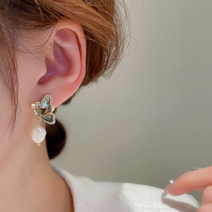 Close-up of butterfly earrings with iridescent shell wings and white pearl drop