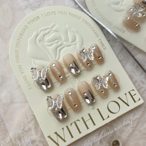 Macro shot of nude pink gradient press-on nails with 3D silver butterflies and rhinestones