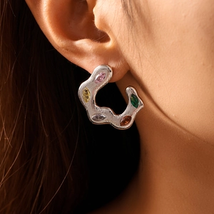 Irregular C-shaped silver earrings with colorful zircon inlay shown on ear model
