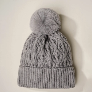 Detailed view of grey knitted beanie with faux fur pompom and textured cable pattern