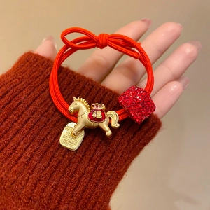 Détail d'un élastique à cheveux rouge avec pendentif cheval doré et strass rouges