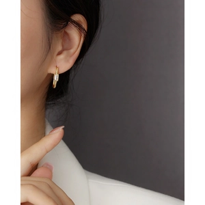 Macro shot of gold U-shaped earring with rectangular zircon on female model's ear