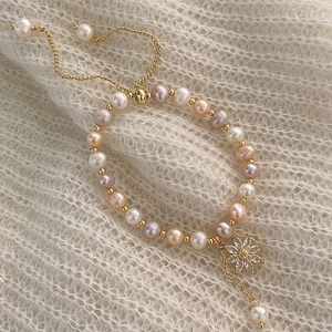 Detail of freshwater pearl bracelet with zircon flower charm on knit background