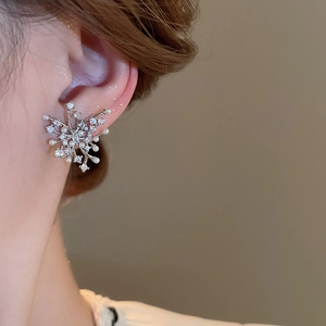 Detailed view of silver zircon and pearl firework earring worn on an earlobe
