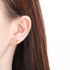 Detailed close-up of heart-shaped gold stud earring with pavé rhinestones on model ear