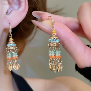 Close-up of bohemian tassel earrings with colorful beads and golden leaf pendants