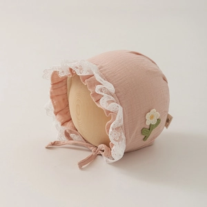 Dettaglio della cuffietta rosa in cotone con pizzo bianco e ricamo di fiori a maglia