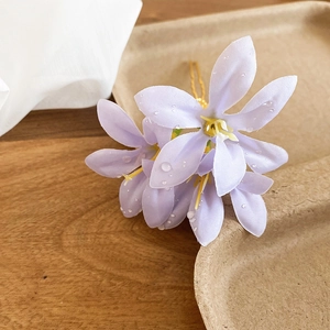 Close-up of lilac fabric flower hair pin with water droplets and golden wire detail