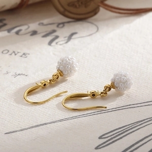 Détail de boucles d'oreilles vintage dorées avec grappes de perles blanches tissées main
