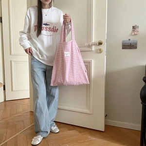 Detailed shot of pink plaid canvas tote bag held by a model in casual casual outfit