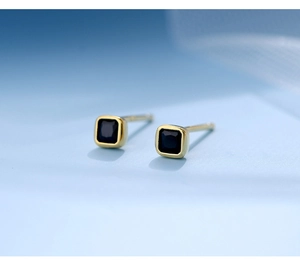 Macro view of mini square gold stud earrings with faceted black gemstones and needles