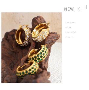 Macro shot of gold-plated C-shape hoop earrings with white and emerald green crystals