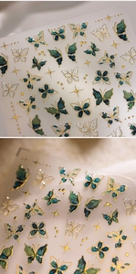 Detailed close-up of emerald green butterfly nail art stickers with gold foil outlines