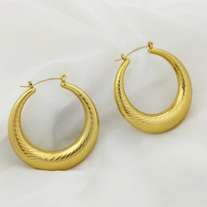 Macro detail of thick gold hoop earrings featuring elegant spiral texture on white fabric