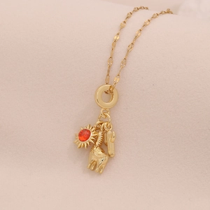 Close-up of gold necklace with red sun, giraffe, and cactus charms on beige fabric