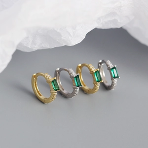 Macro shot of gold and silver rectangle green zircon hoop earrings on textured paper