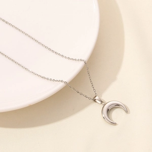 Dettaglio del ciondolo a luna in argento lucido su una sottile catena dallo stile minimal