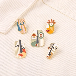 Detailed view of five colorful Picasso-style abstract face enamel pins on fabric