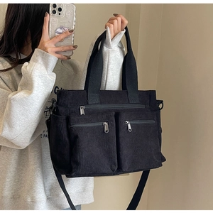 Mirror selfie showing a black corduroy tote bag with dual front zipper pockets