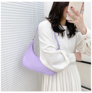 Detail view of a minimalist light purple nylon baguette bag worn by a model in a white dress