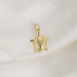 Detailed view of a golden sea turtle pendant featuring zircon inlay on white silk fabric