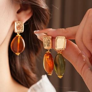 Detail showing square gold studs with amber and olive green resin teardrop pendants