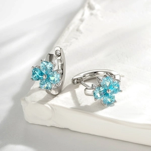 Copper zircon clover hoop earrings with light blue stones on silk and plaster background