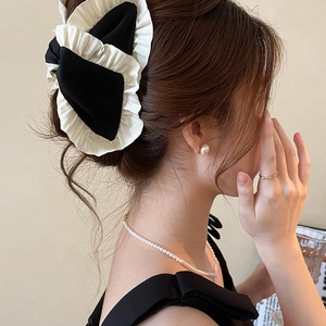 Elegant black and cream pleated fabric bow hair clip worn by a model in a side view
