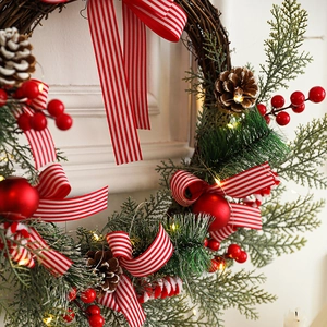 Illuminated Christmas wreath with pine cones red berries and striped ribbon bow decoration
