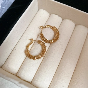 Detailed macro view of gold hoop earrings with textured scale-like weaving in a jewelry box