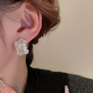 Macro shot of silver textured pleated earrings showing layered metallic lines on a model