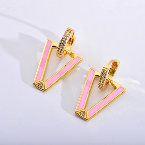Macro shot of V-shaped gold earrings with pink enamel inlay and sparkling rhinestones
