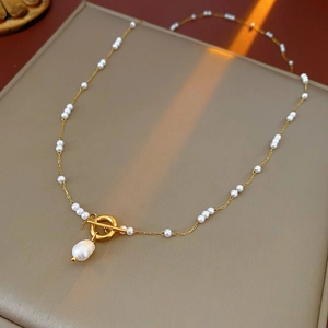 Détail d'un collier en titane doré avec petites perles et pendentif perle baroque t-bar