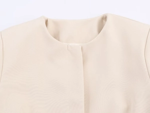 Detail eines beigen Rundhals-Blazers mit gewebter Textur und verdeckter Knopfleiste