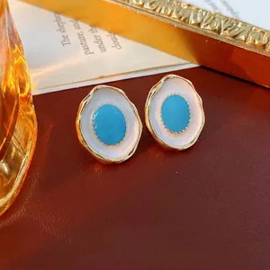 Vintage oval turquoise enamel earrings with gold wavy edge on a retro leather background