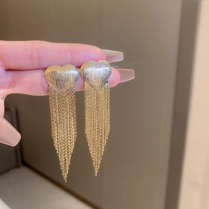 Macro shot of gold heart tassel earrings with brushed metal finish and long chains