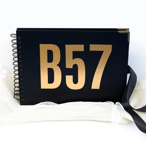 Detail of a black notebook with gold foil B57 lettering on white lace fabric