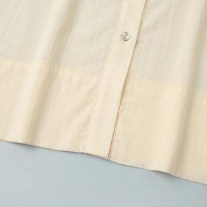 Detail of cream linen shirt featuring a pearl button and fine stitching texture