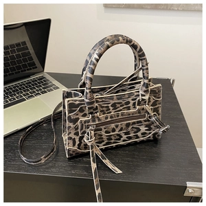 Dettaglio borsa leopardata con cerniera a nappa e laptop su scrivania scura