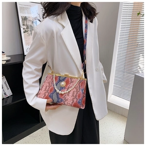 Détail du sac à main serpent rose et bleu avec chaîne de perles sur blazer blanc