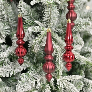 Three red metallic teardrop Christmas ornaments hanging on a snowy tree branch