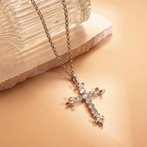 Macro view of rhinestone-studded silver fleur-de-lis cross pendant on a textured stone base