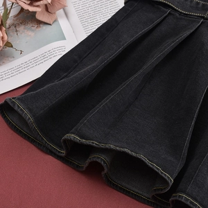 Detail-Makroaufnahme des schwarzen Denim-Faltenrocks mit gelben Kontrastnähten und Textur