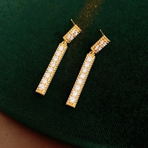 Vue détaillée de boucles d'oreilles frangées dorées avec zircons sur tissu vert texturé