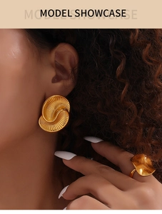 Detailed shot of golden spiral shell earrings and irregular wave ring with metallic luster
