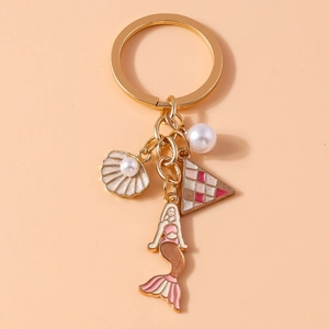 Detail shot of golden mermaid keychain with pearl shell and star pendants on peach background